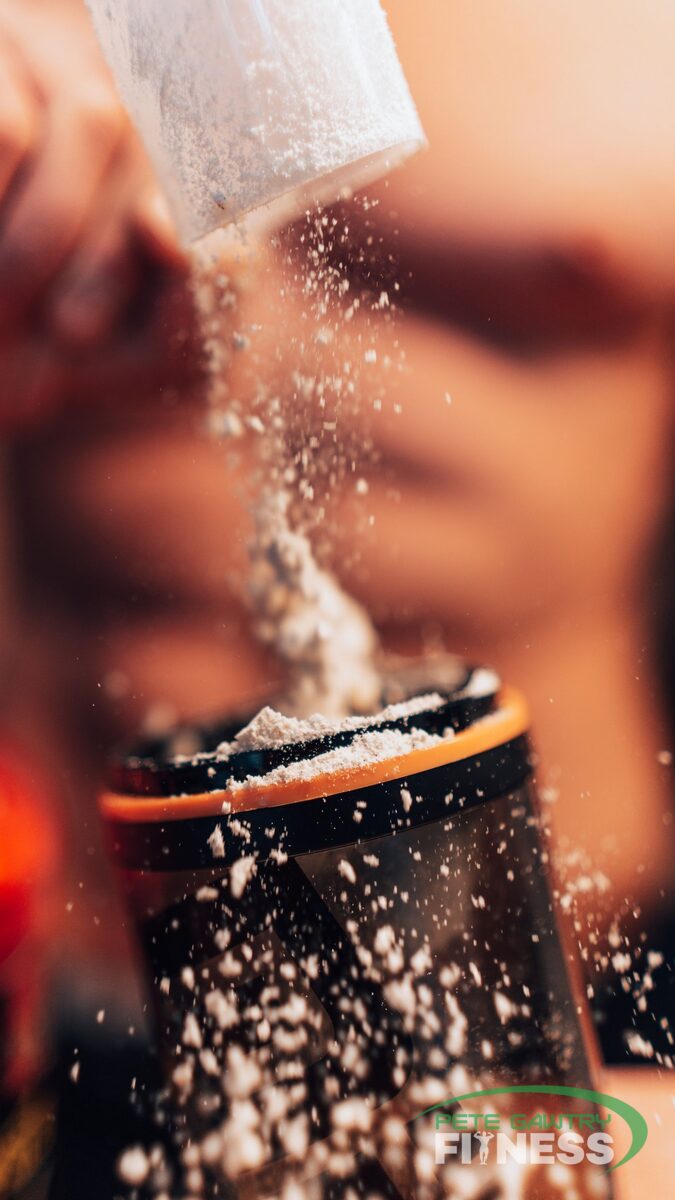 A scoop of plain creatine powder going into a shaker — 3 to 5 grams of monohydrate a day is the whole routine