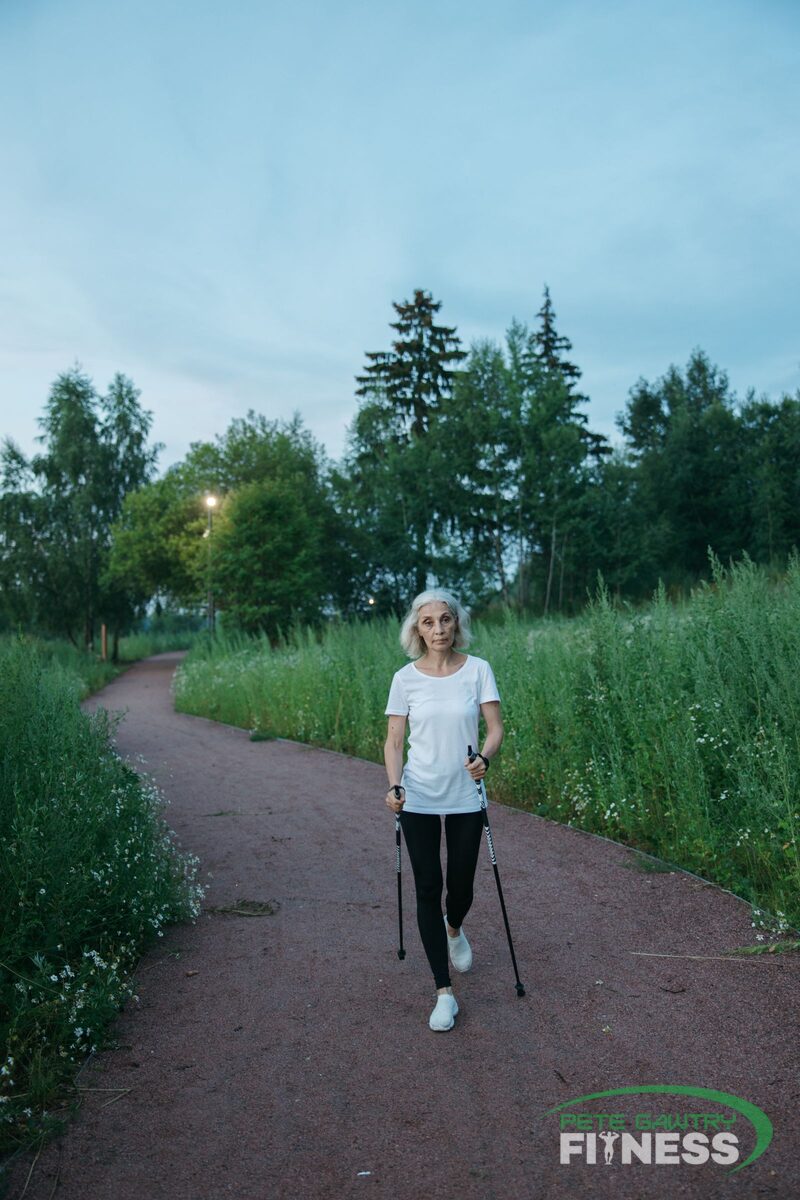 A woman walking briskly along a green park path with walking poles — the daily habit that looks after your heart and head
