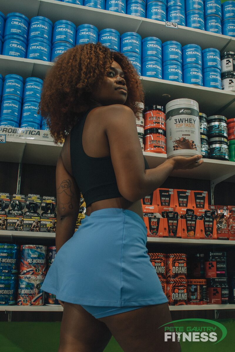 A woman weighing up supplement tubs in the shop — the plain creatine next to the pink one is the same powder for less