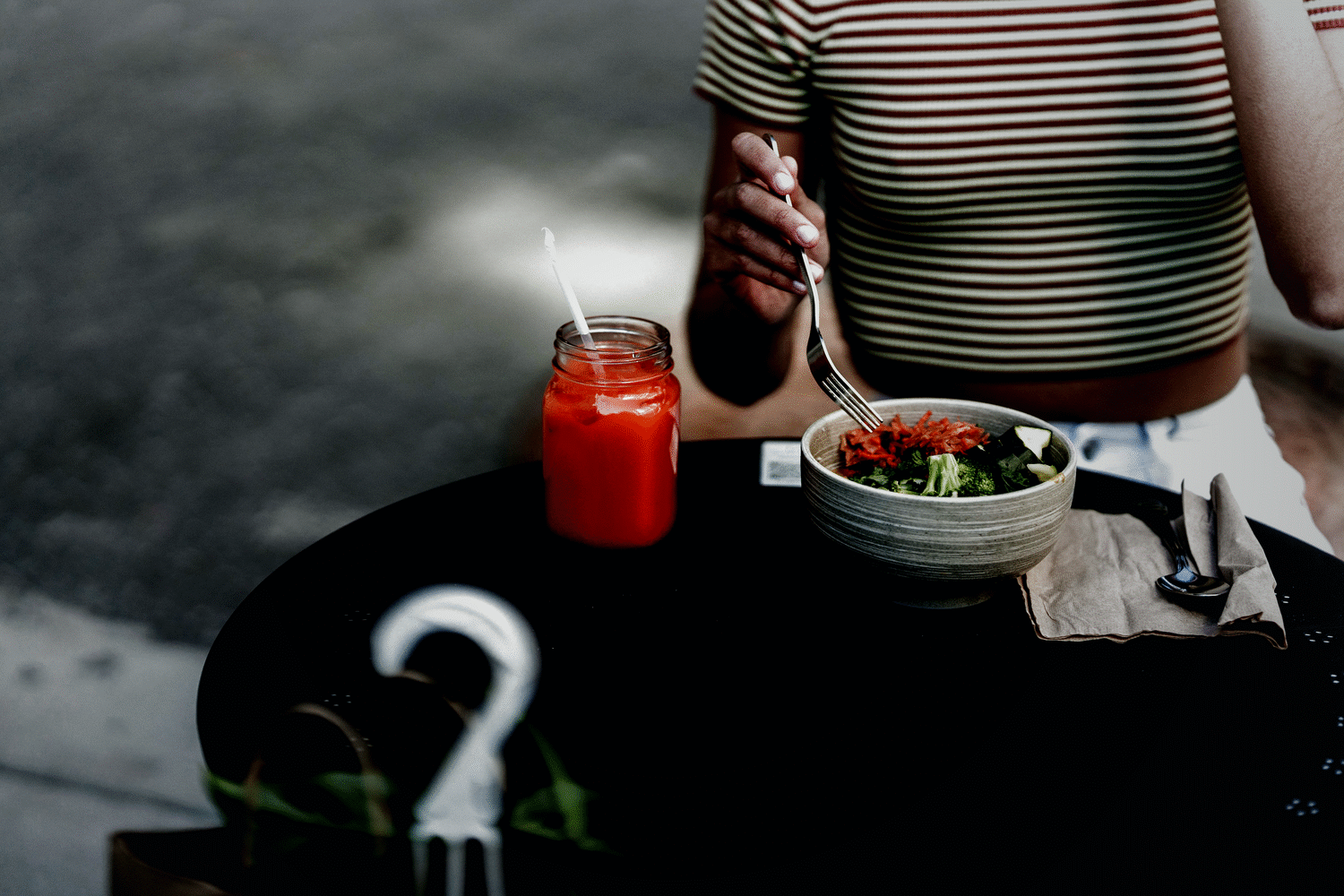 A woman eating a fresh vegetable salad bowl at a table