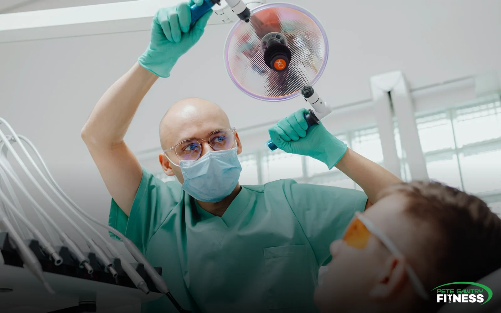 A dentist in surgical scrubs working over a patient reclined in the chair under the overhead light