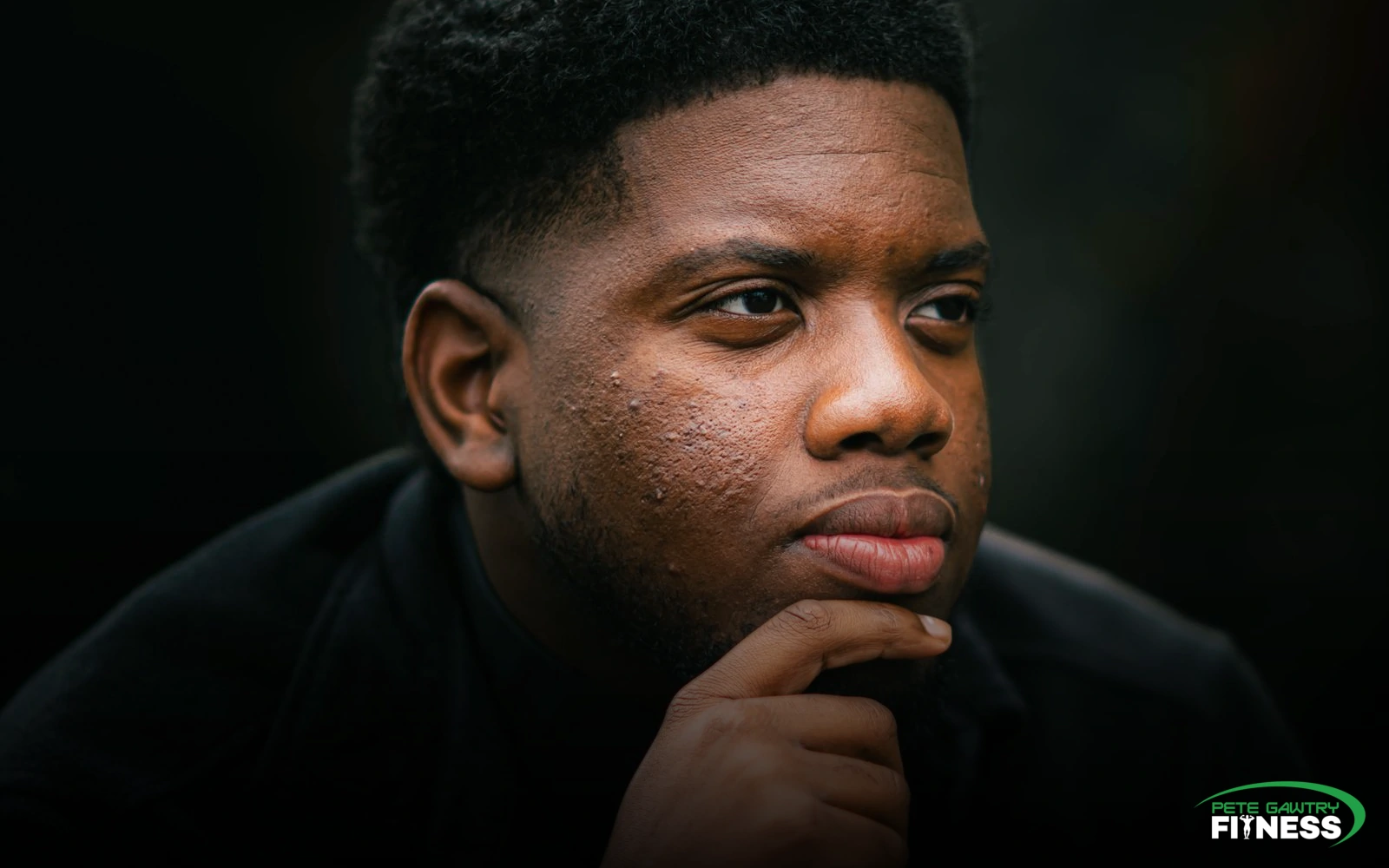 A thoughtful man in low light, hand resting on his chin, looking calmly into the distance