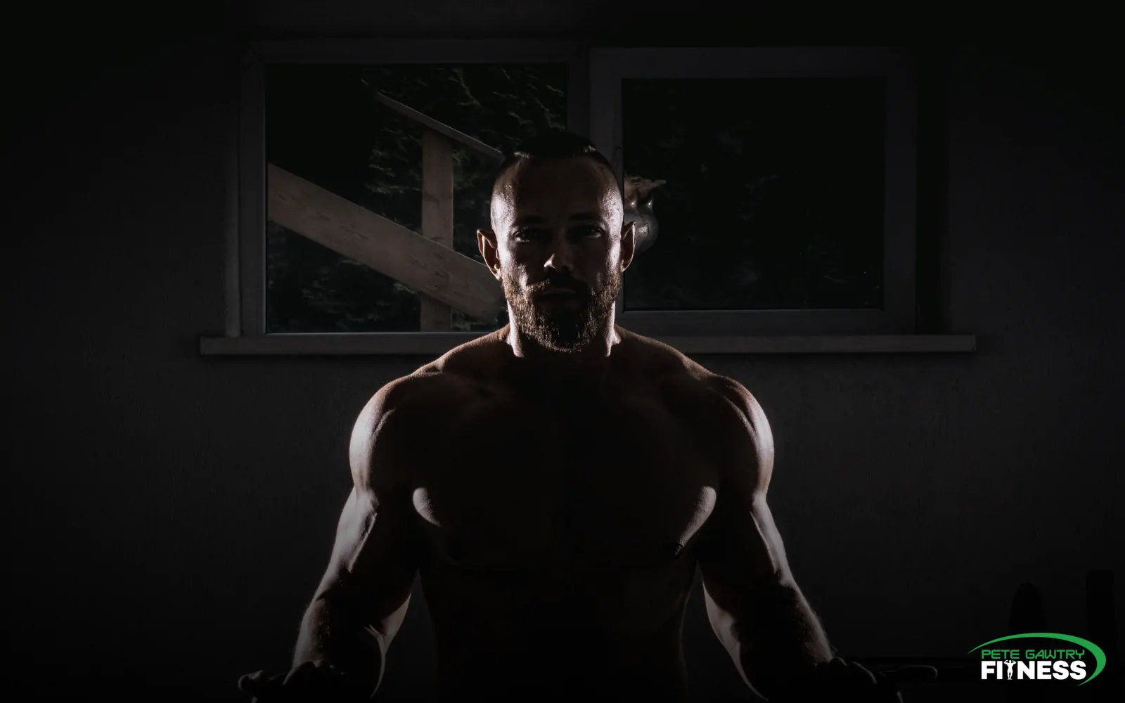 A lean, muscular man training with kettlebells in a dark gym — sweating and the boring fundamentals are your everyday detox