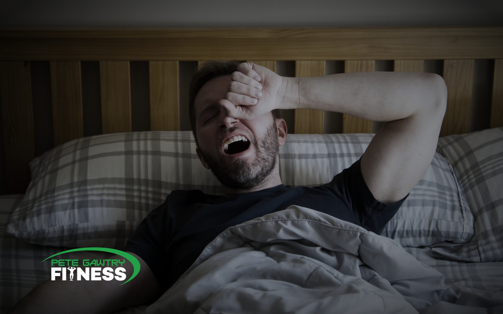 A man sitting on the edge of his bed first thing in the morning, yawning and rubbing his eyes