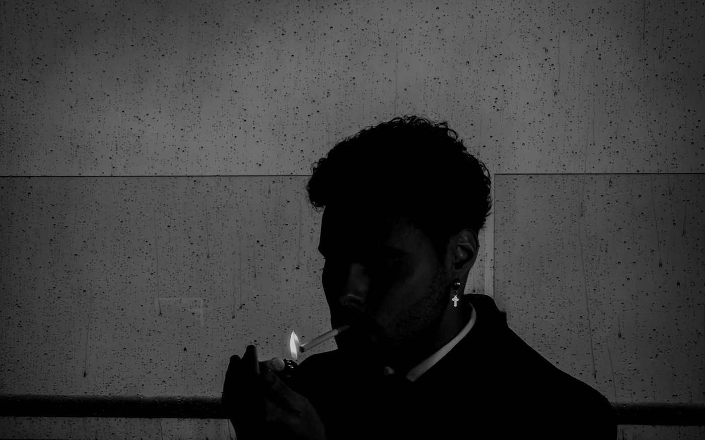 A man lighting a cigarette against a concrete wall at night