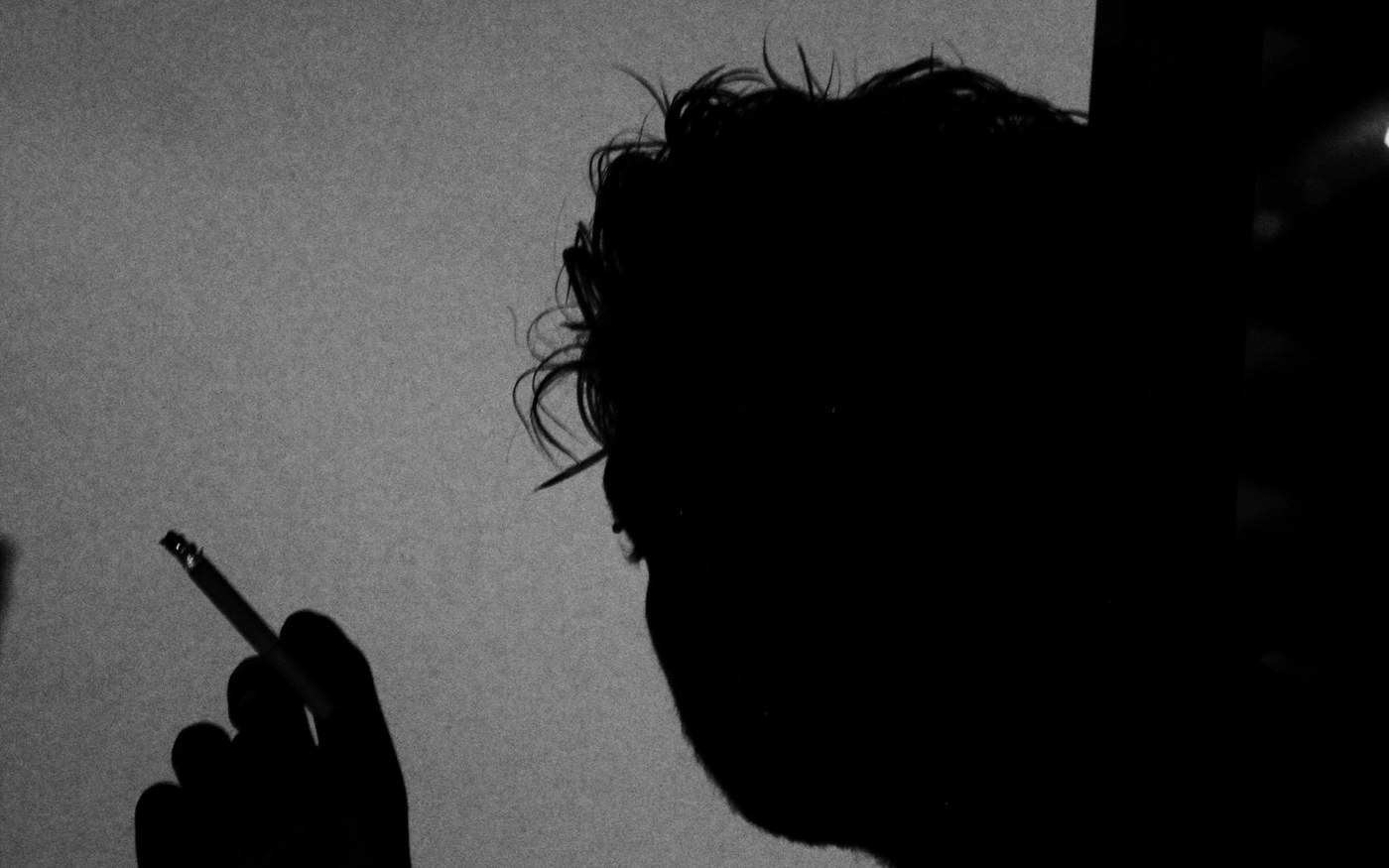 Silhouette of a person holding a cigarette in near darkness