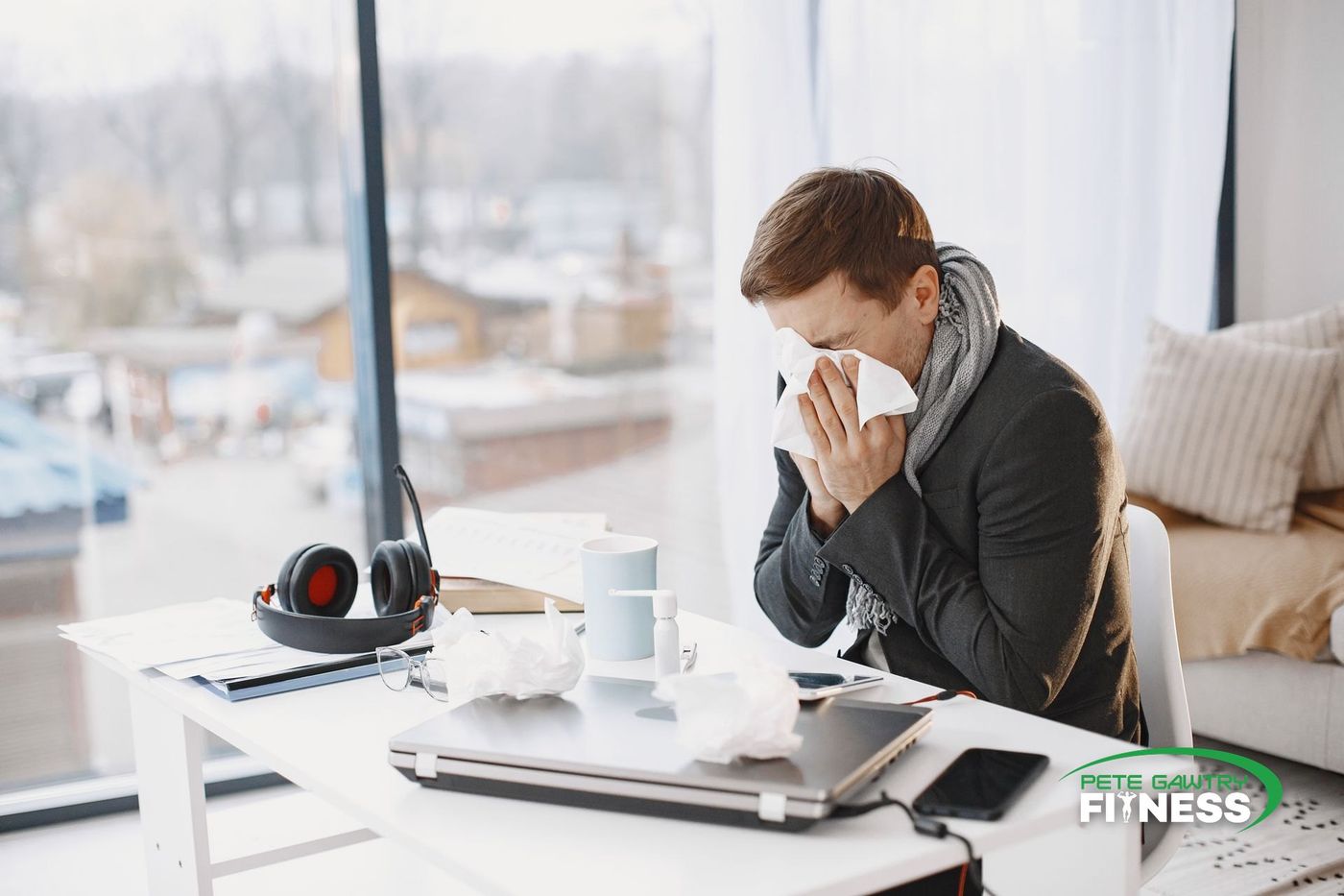 A man blowing his nose at his desk, surrounded by used tissues