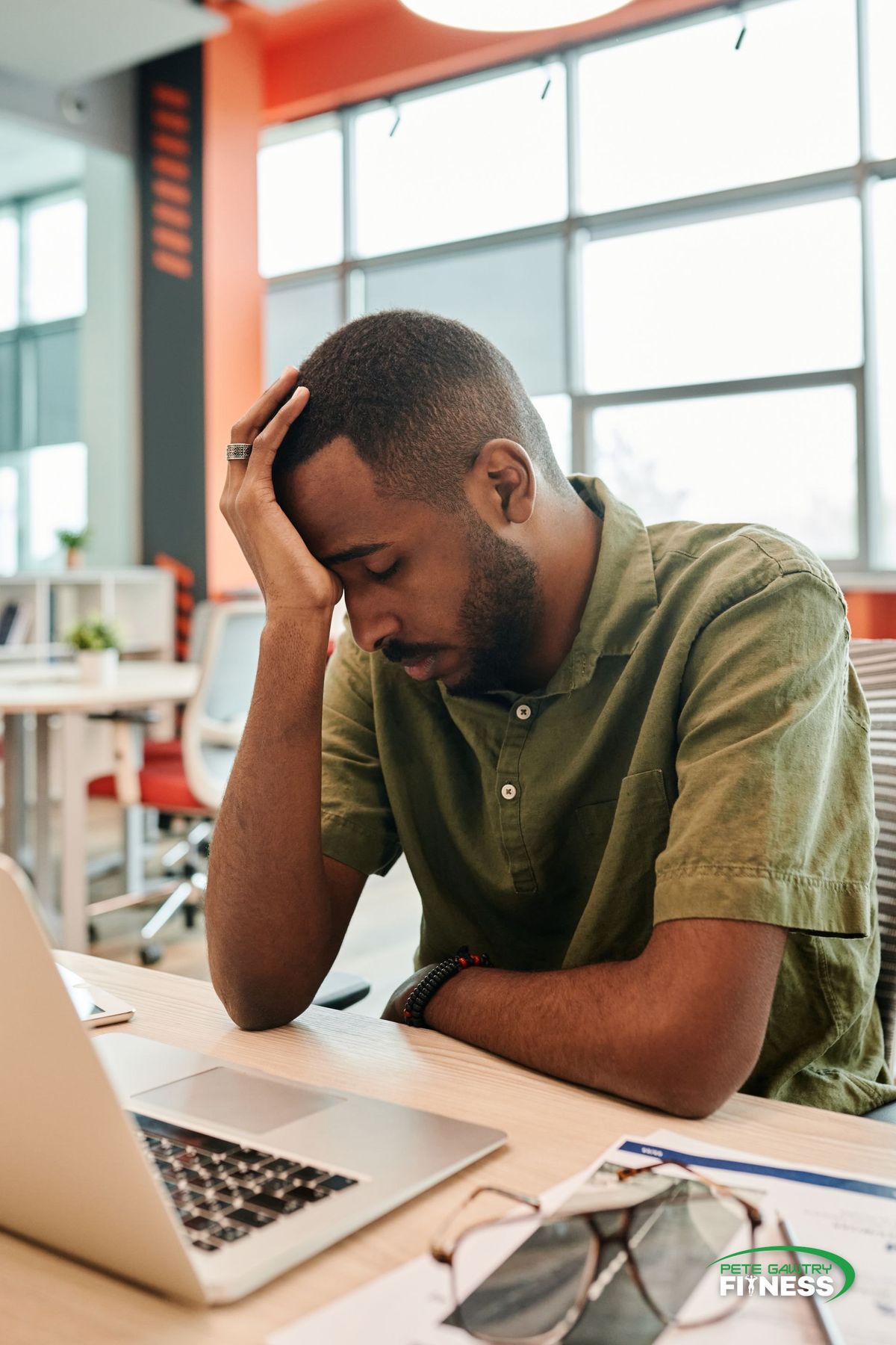 A man sitting at a laptop in an open-plan office with his head in his hand