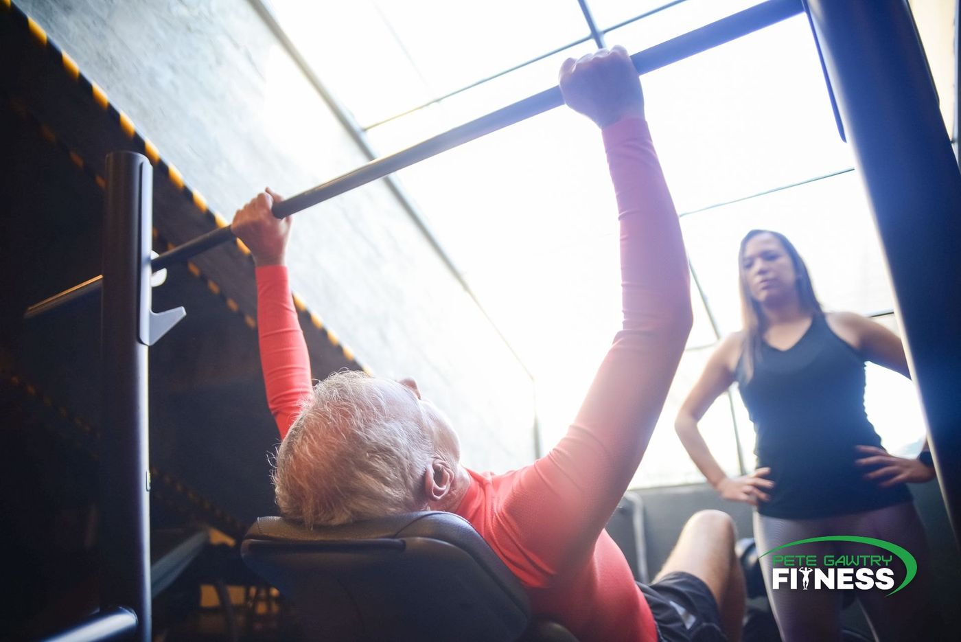 An older man bench pressing while a personal trainer spots him