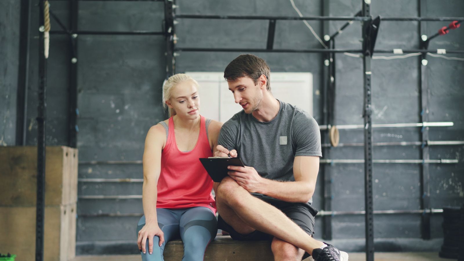 A personal trainer going through a plan on a clipboard with a client sitting in a gym