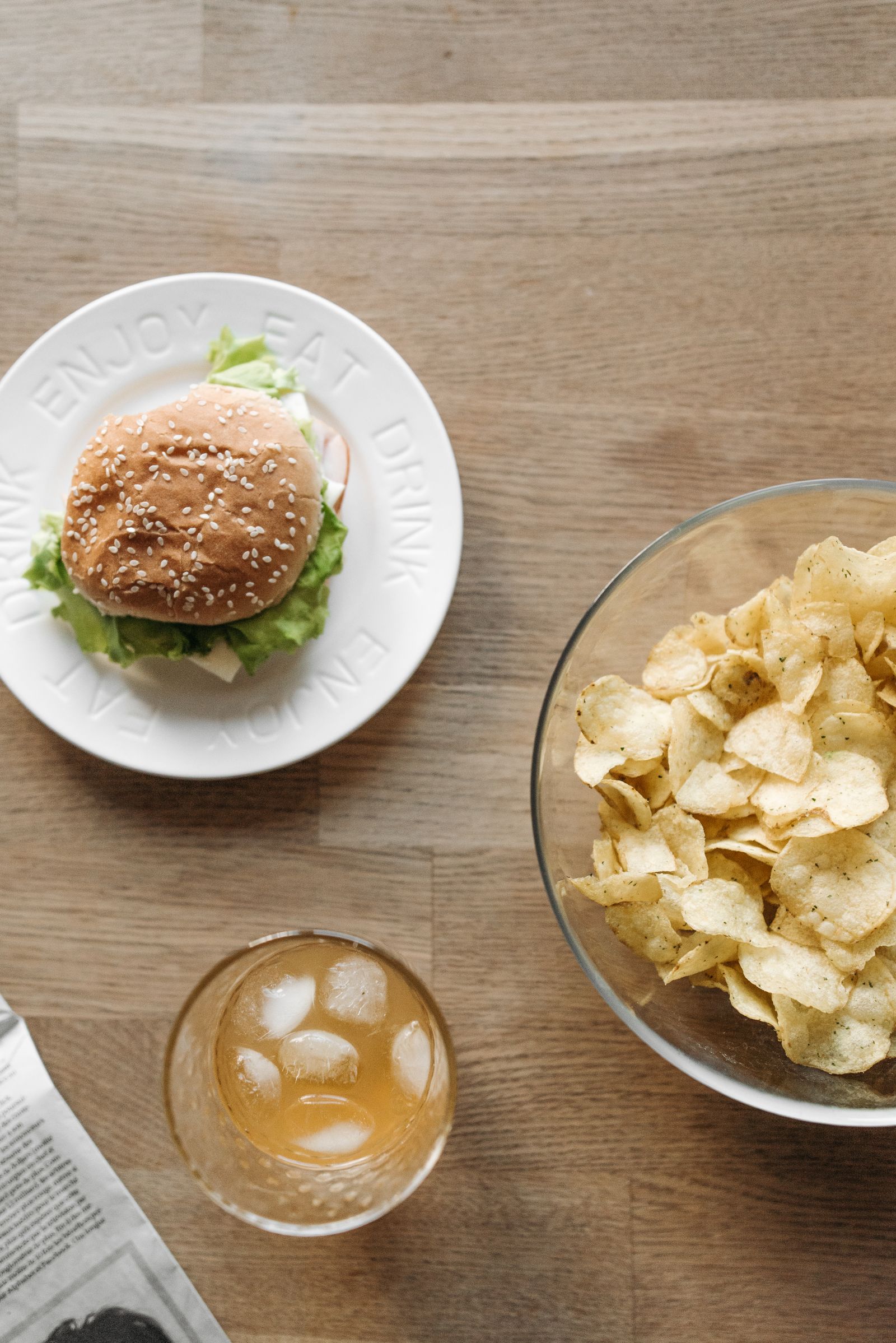A burger on a plate next to a bowl of crisps and a glass of fizzy drink on a wooden table