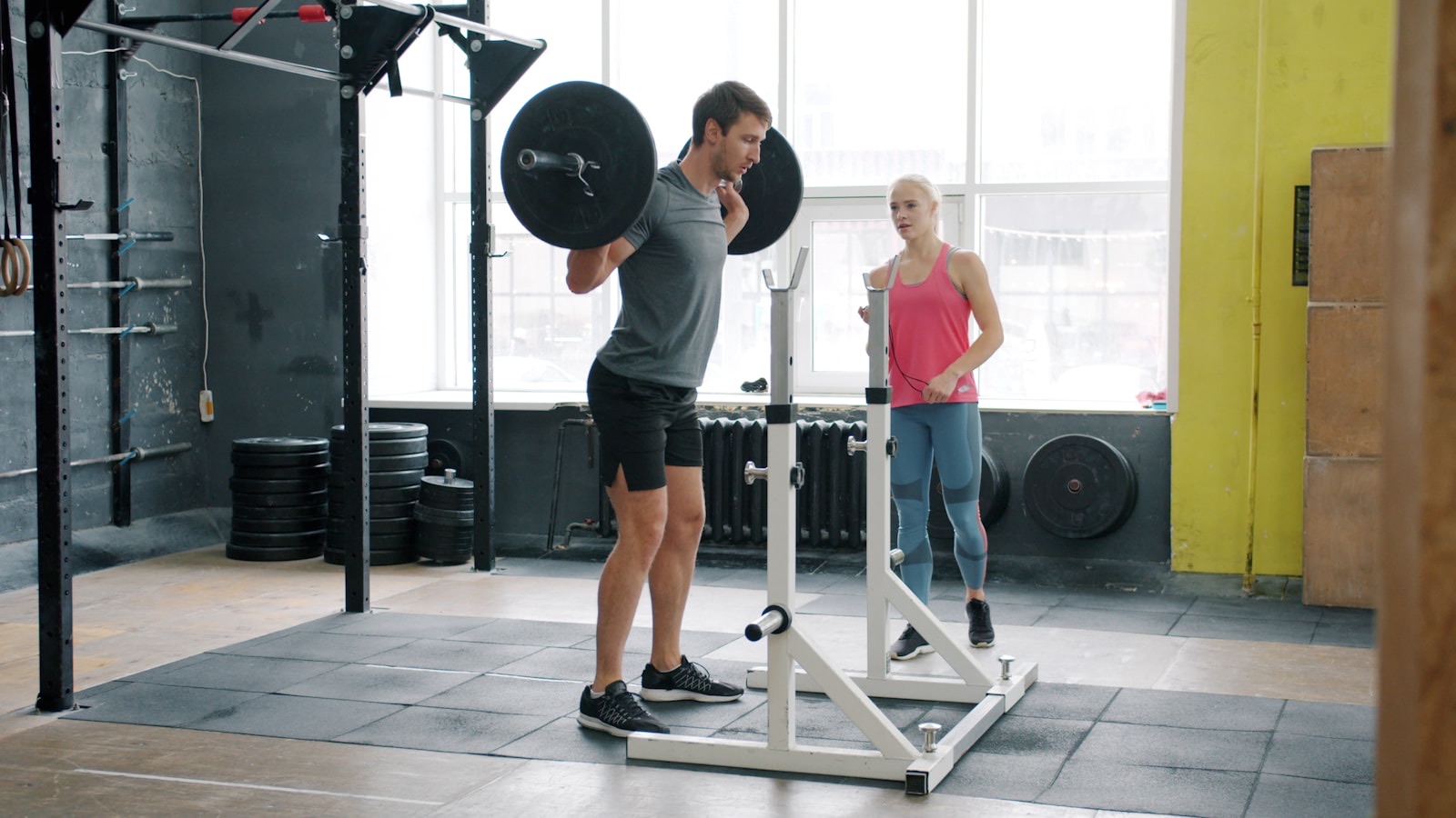 A coach watching a client's barbell back squat in a gym